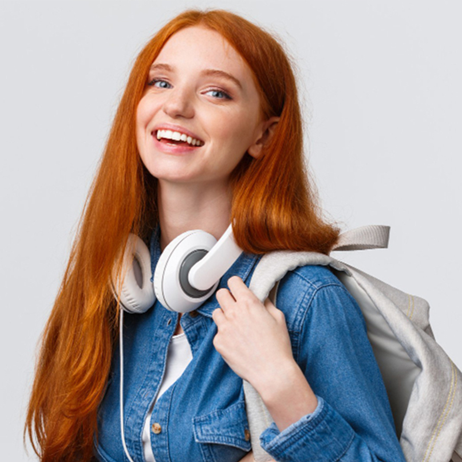 college life modern lifestyle education concept cheerful good looking redhead female student with foxy long hair wearing headphones neck backpack smiling camera